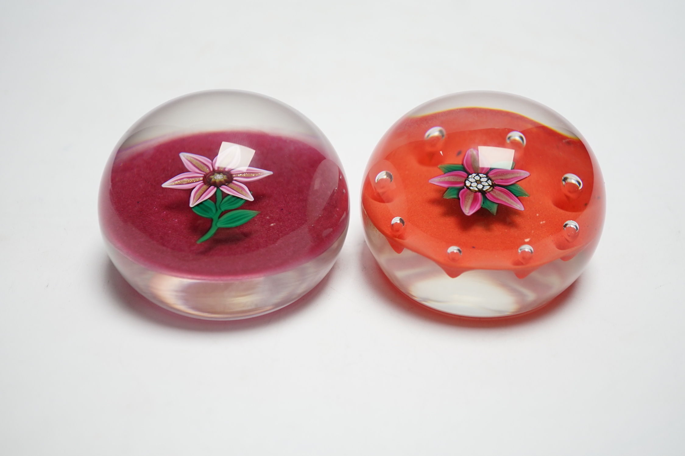 Two Paul Ysart glass ‘flower specimen’ paperweights, both Harland period, the first with a pink and aventurine flower with green stem on a raspberry ground, H cane to base, PY label, 7cm, The second with a pink and adven